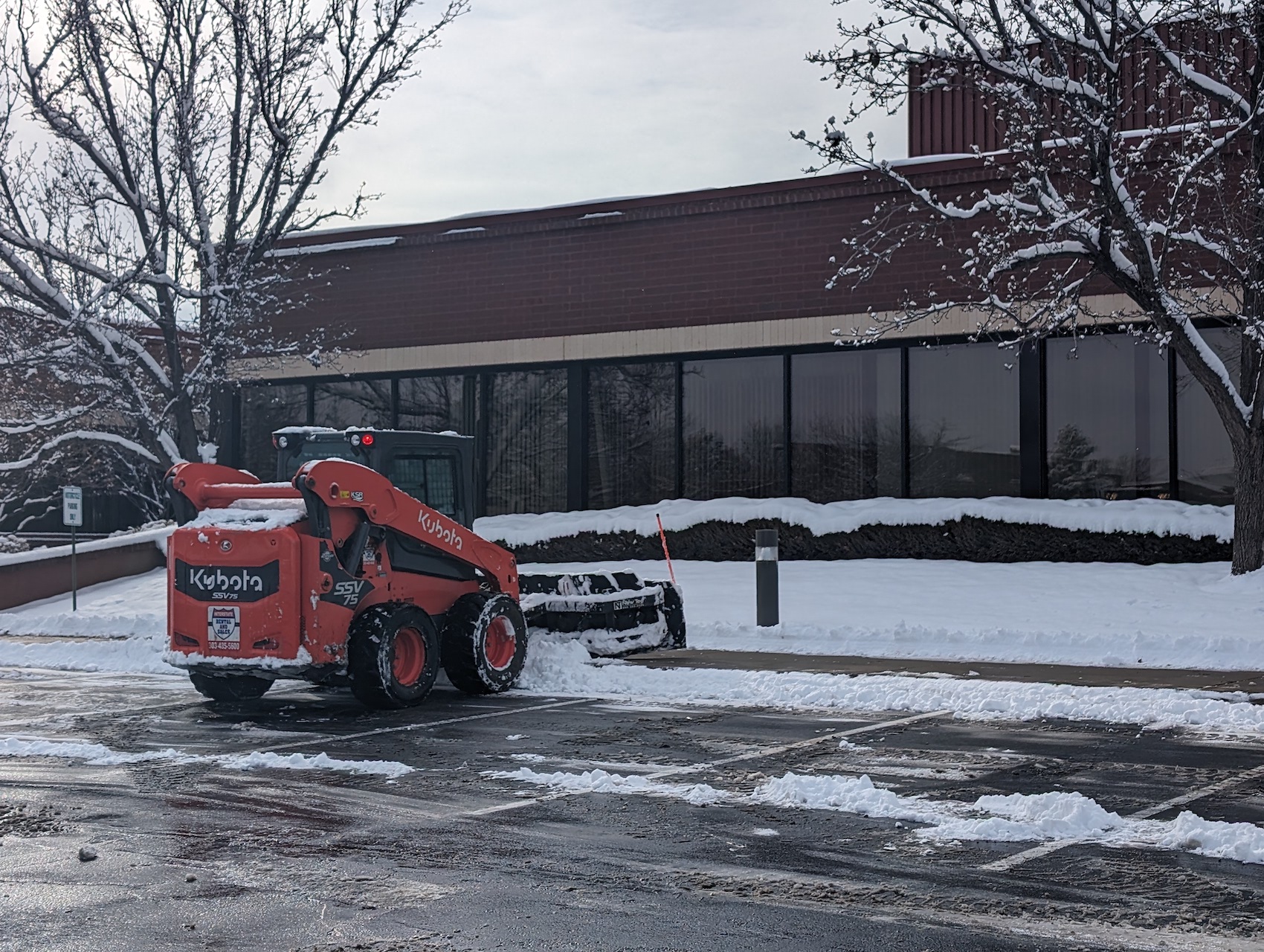 red snow plow removing snow from parking spots 